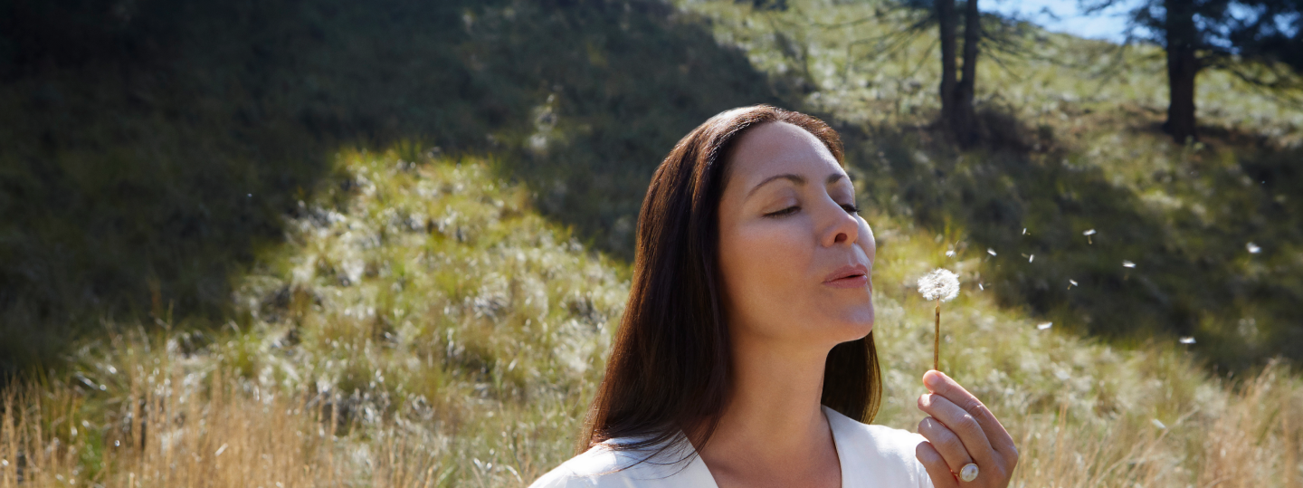 A woman blowing a dandillion in a field